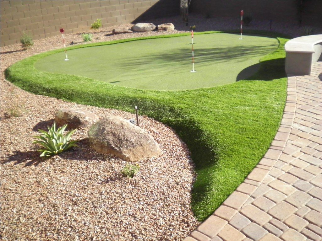 A brick walkway leading to a green putting green