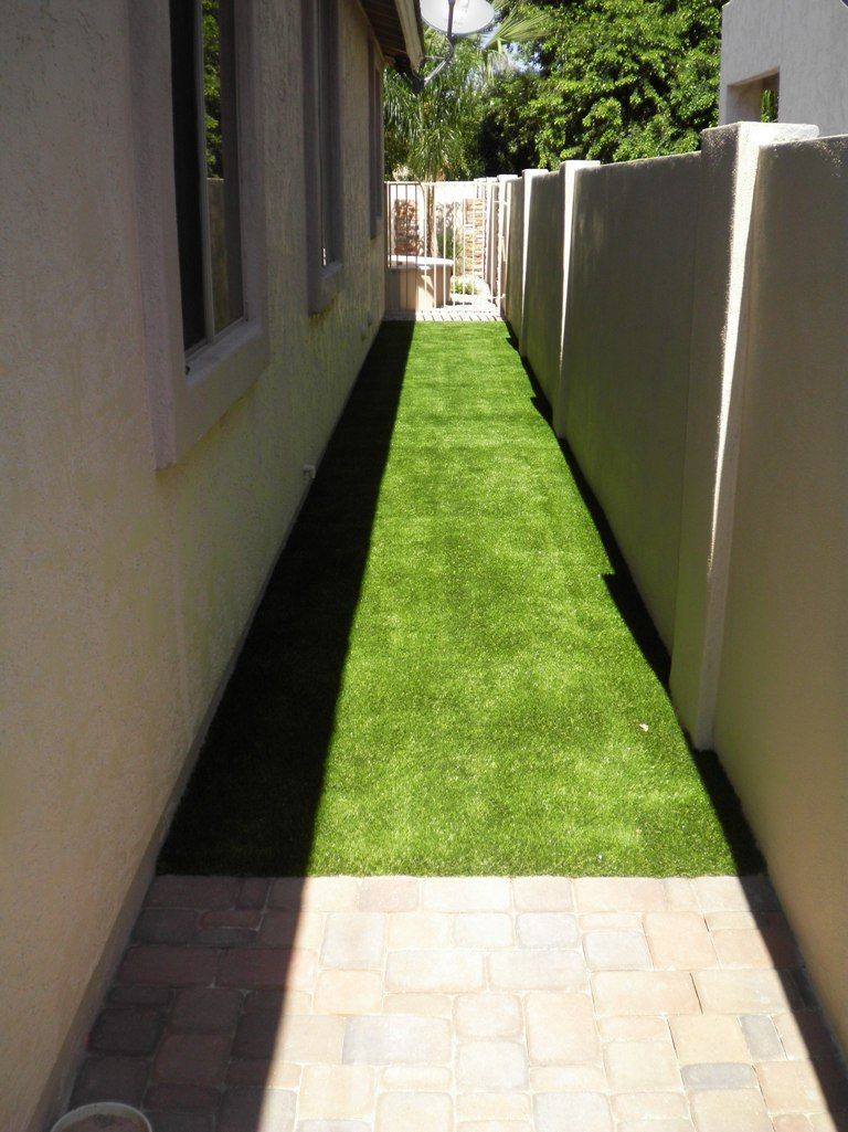 A narrow walkway leading to a house with a lush green lawn