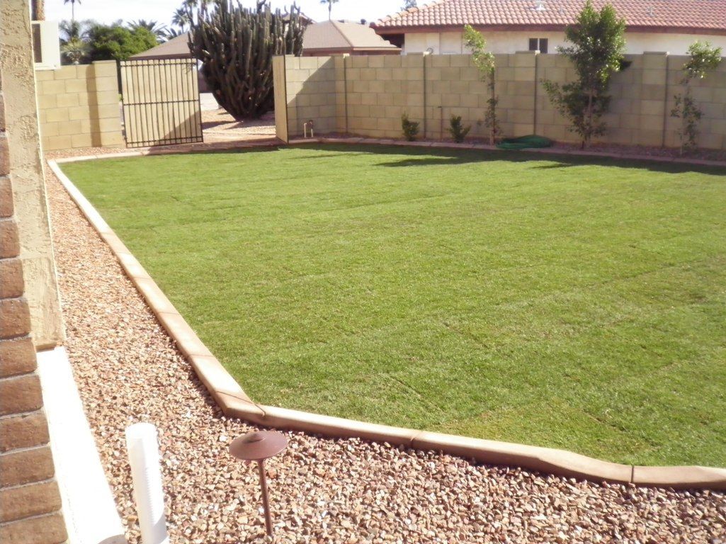 A lush green lawn is surrounded by gravel and a fence