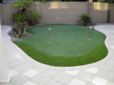 A putting green in a backyard with a brick walkway