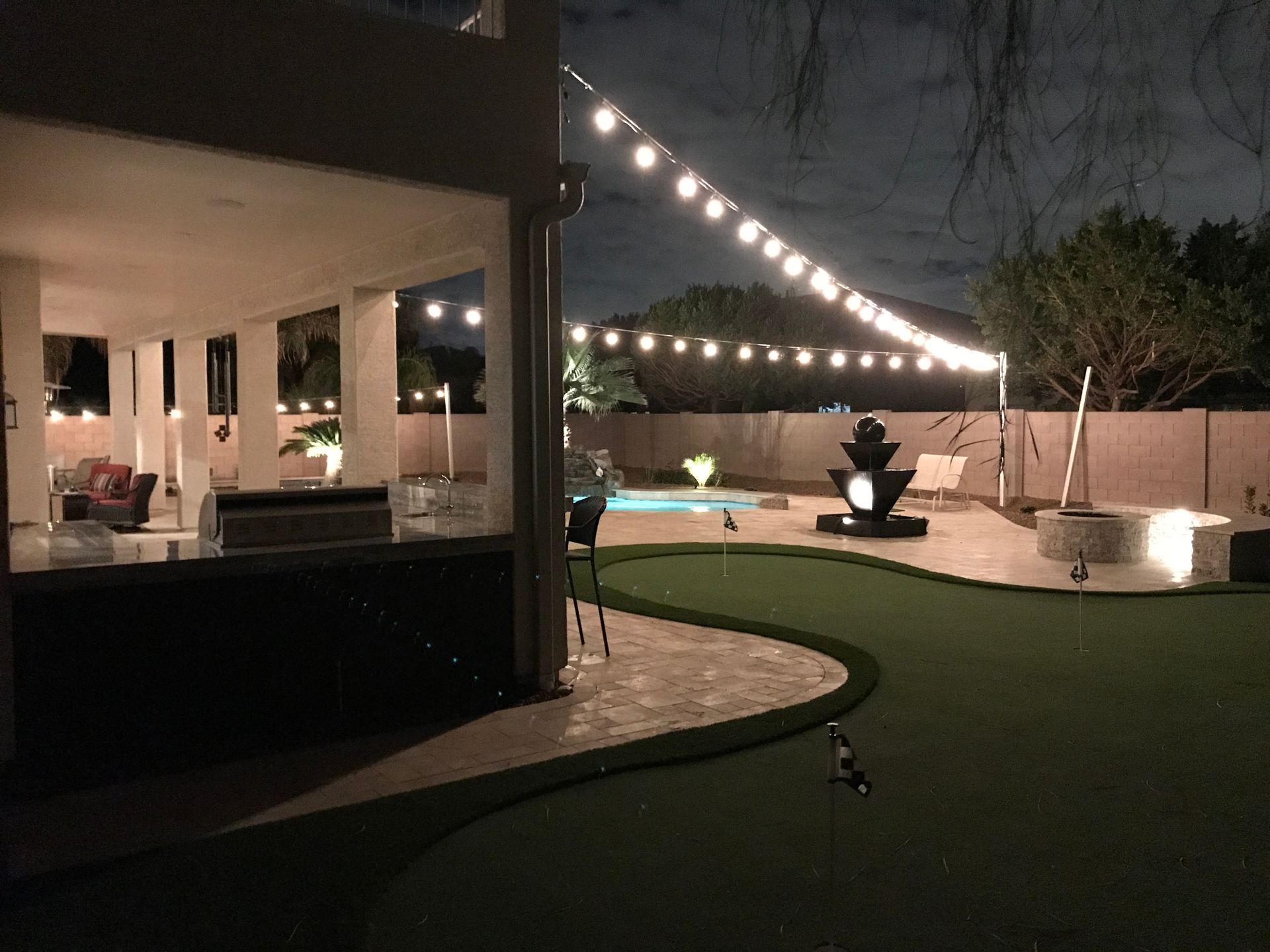 A backyard with a swimming pool and a putting green at night.