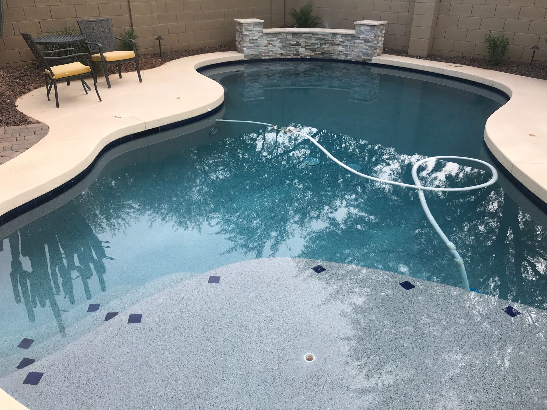 A large swimming pool with a table and chairs in the background