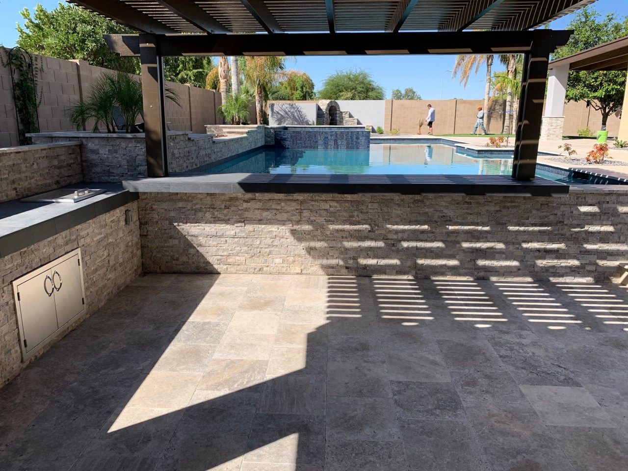 A patio with a pergola overlooking a swimming pool.