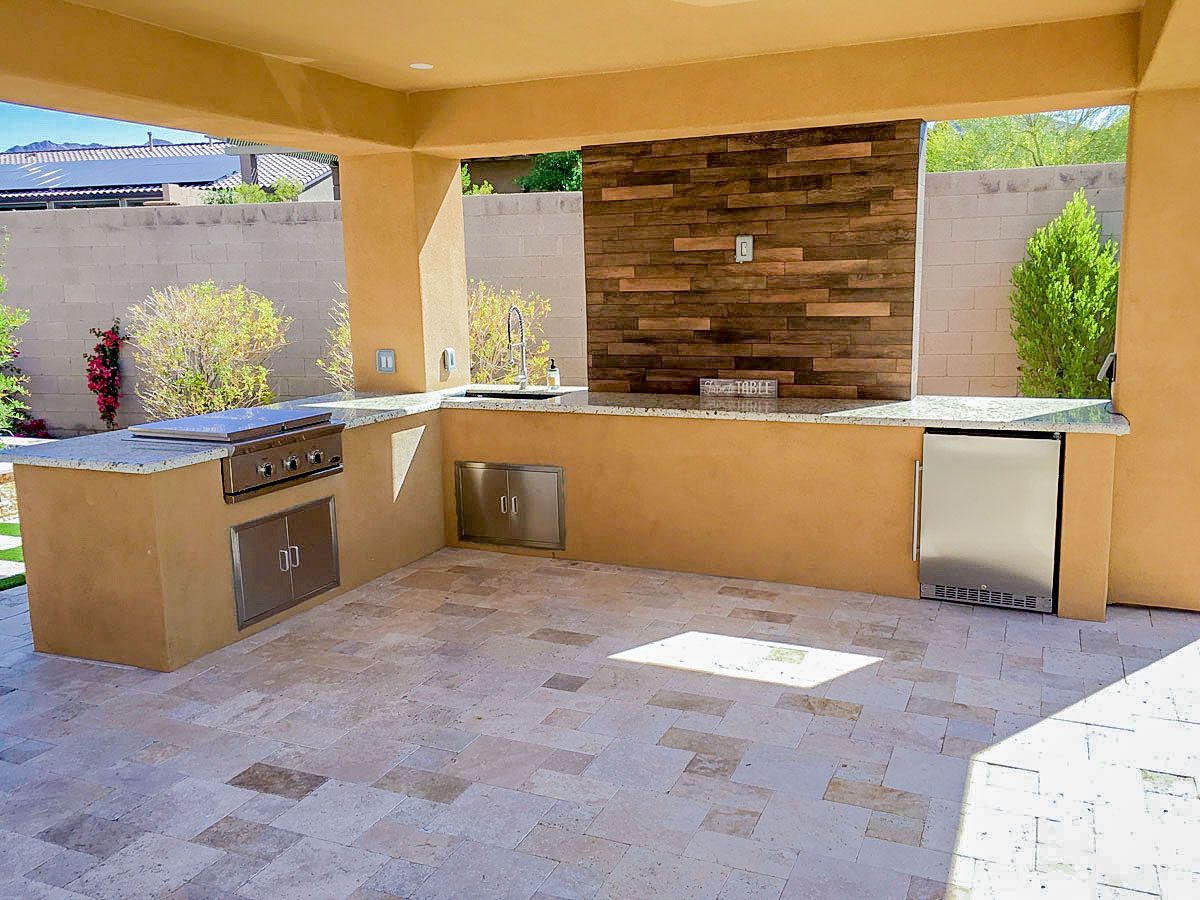 A large outdoor kitchen with stainless steel appliances and a stone wall.