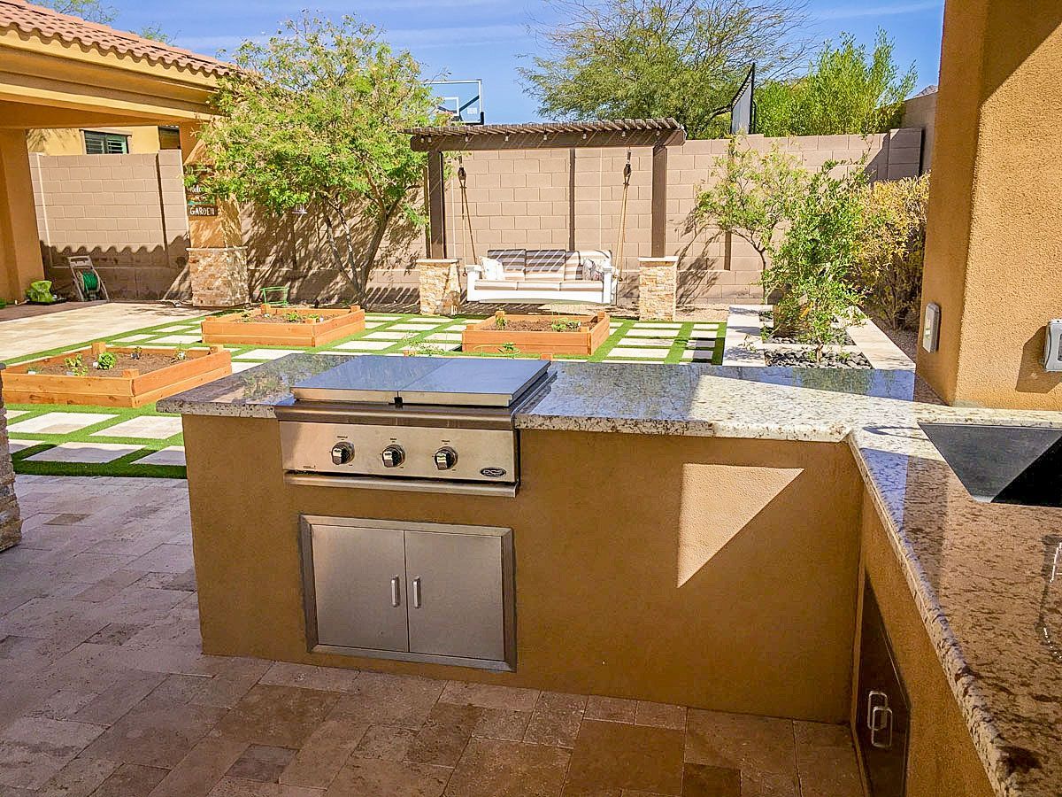 A kitchen with a grill and a sink in a backyard.