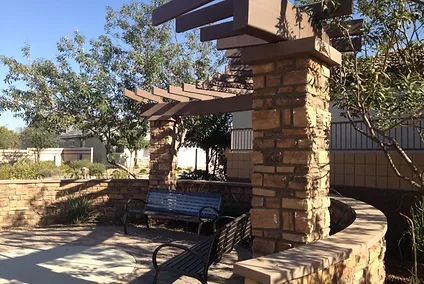 A bench under a pergola in a park with trees in the background