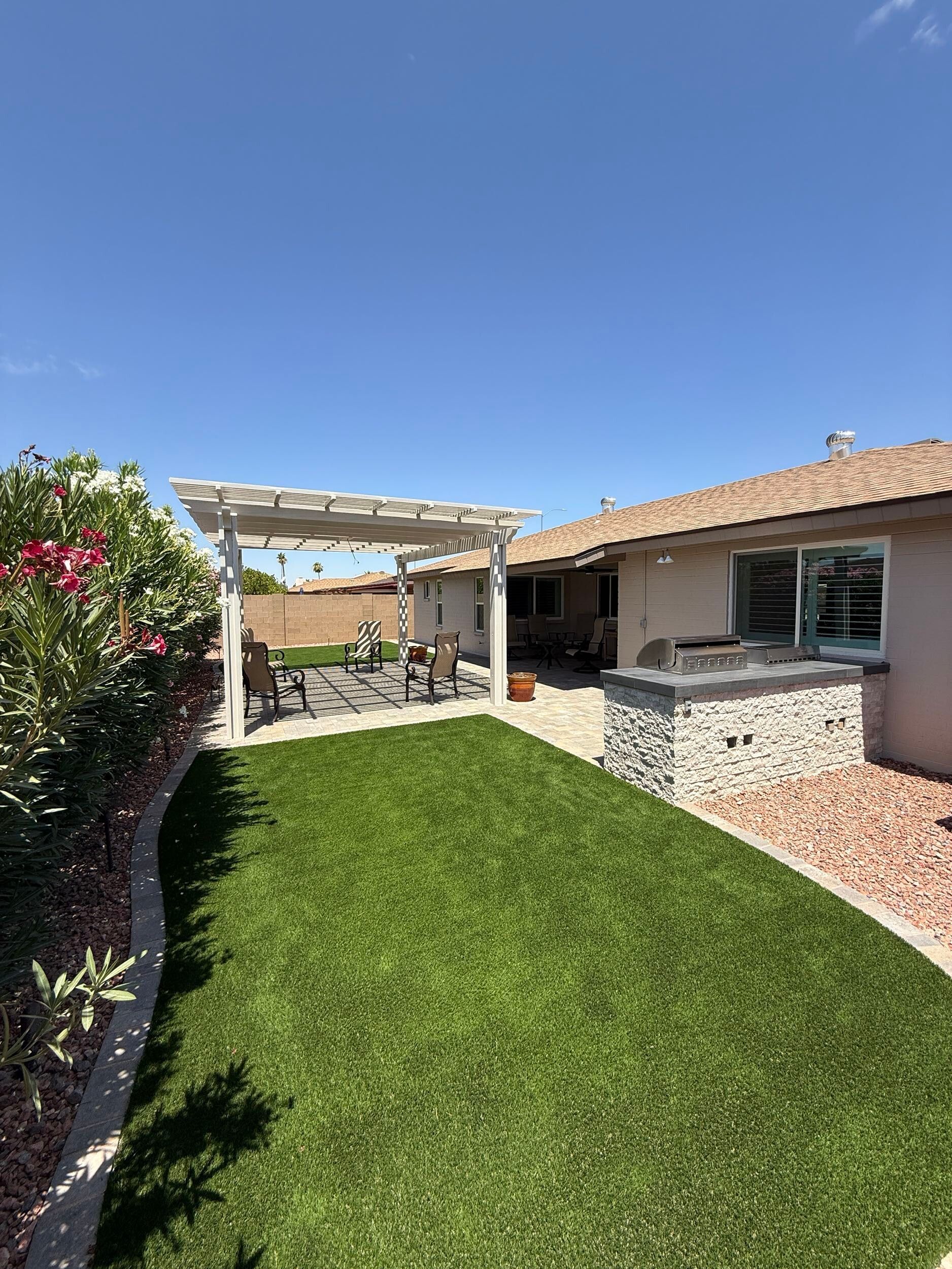 Green backyard with a pergola and built-in grill under a clear blue sky.