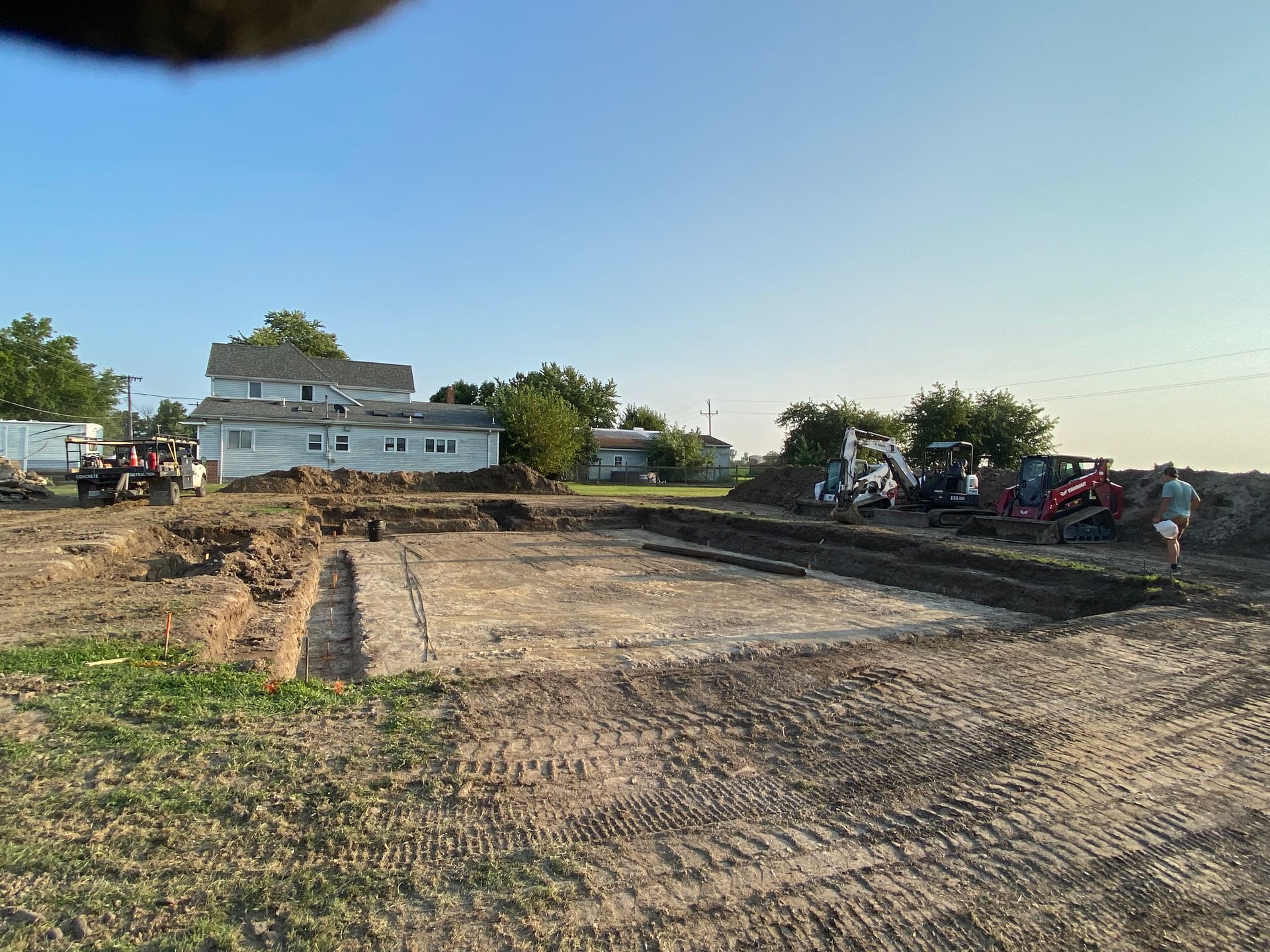 A group of construction vehicles are working on a dirt field in front of a house.
