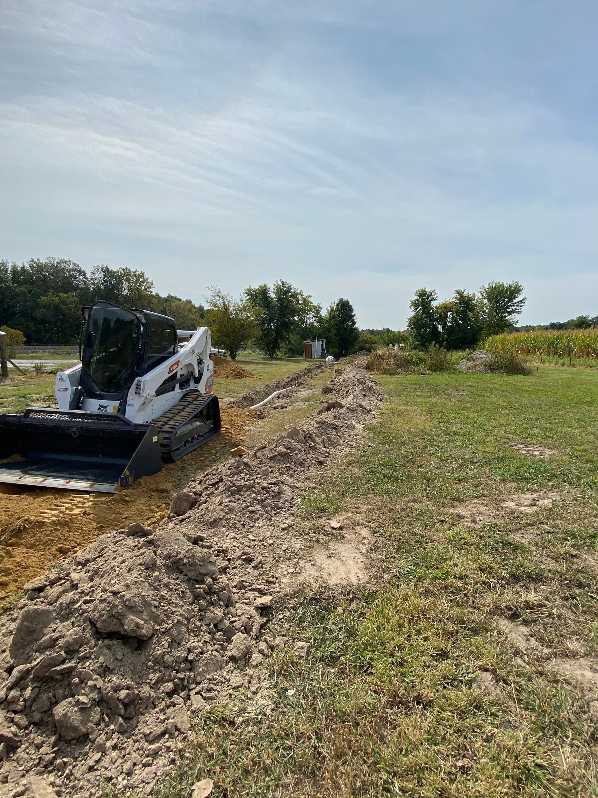 A bobcat is digging a trench in a field.