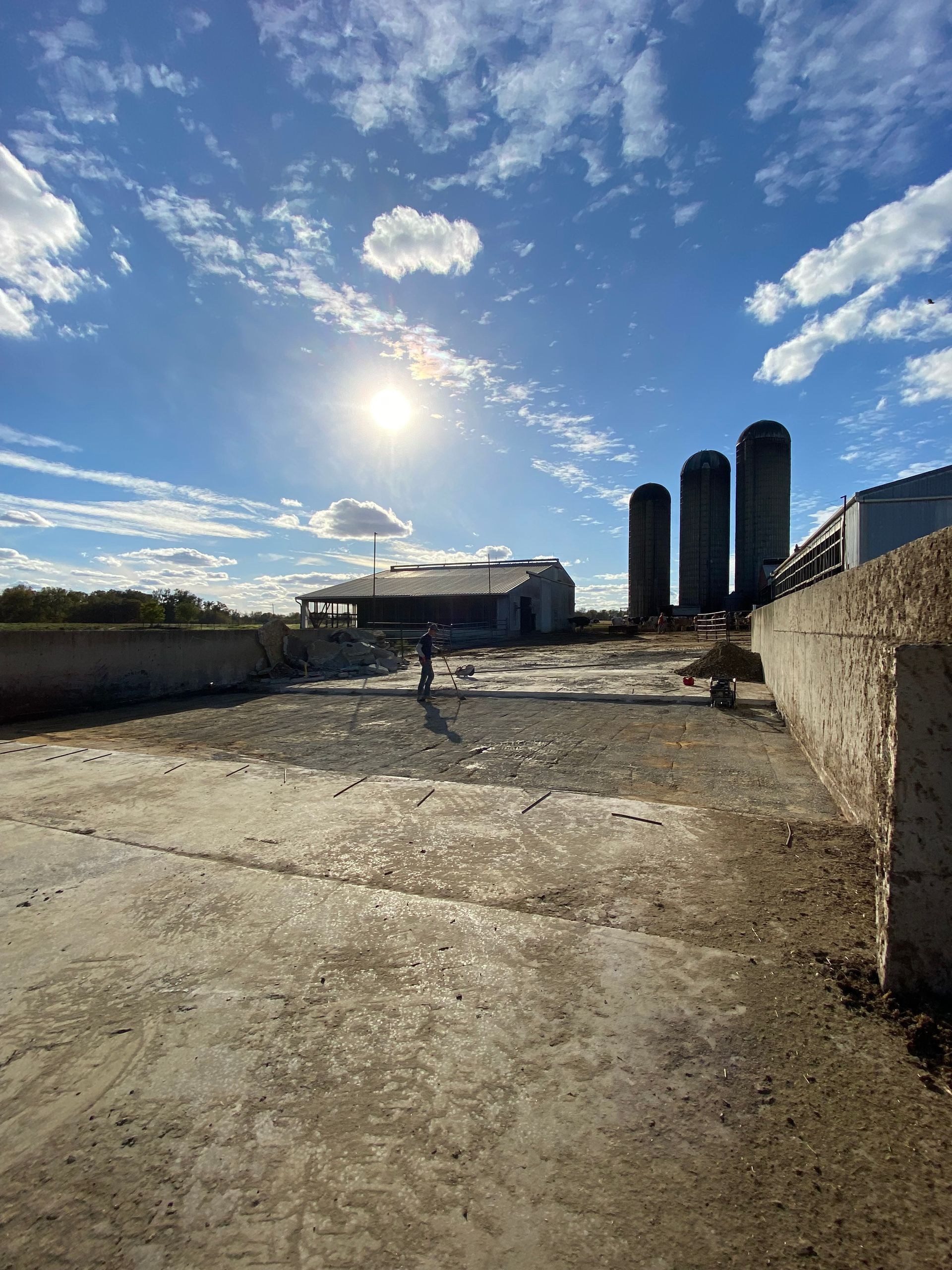 A large dirt field with a barn and silos in the background.