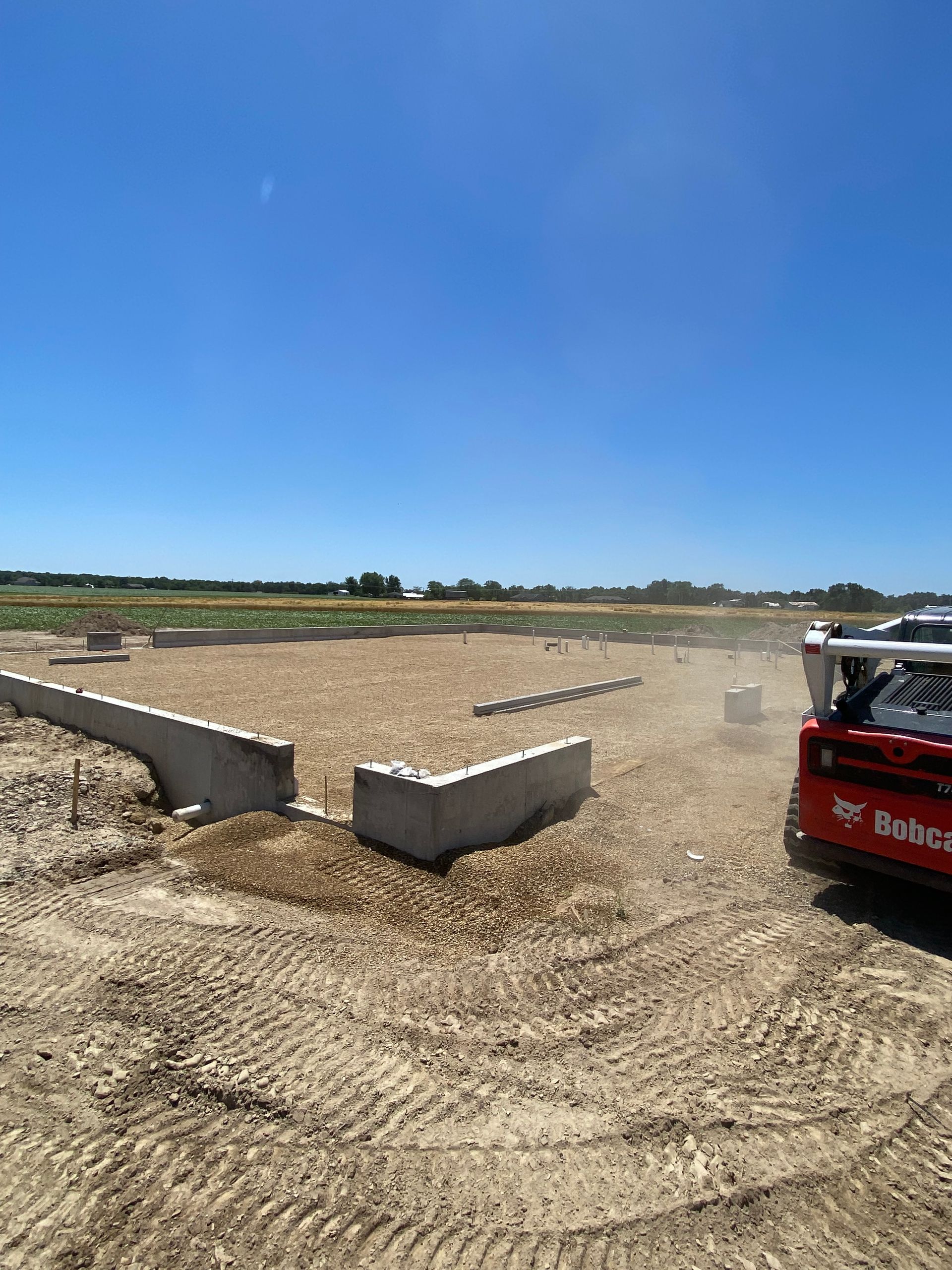 A red bobcat is driving through a dirt field.