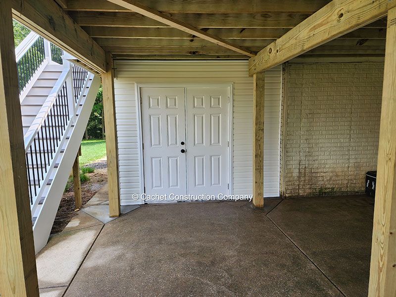 Under deck storage area with double white doors, brick wall, and stairs.