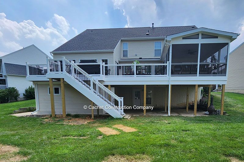 Back view of a two-story beige house with a deck and screened porch on a grassy yard.