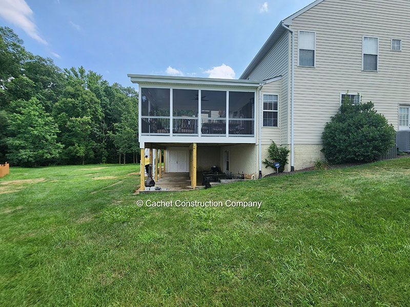 Screened porch attached to a two-story beige house; green lawn in the foreground, blue sky.