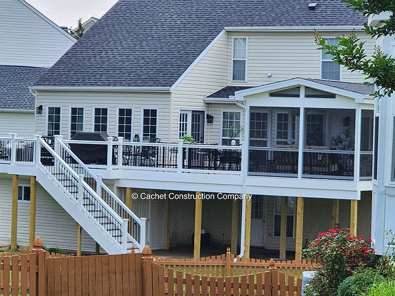 White deck with stairs attached to a light beige two-story house; a screened porch is on the right.