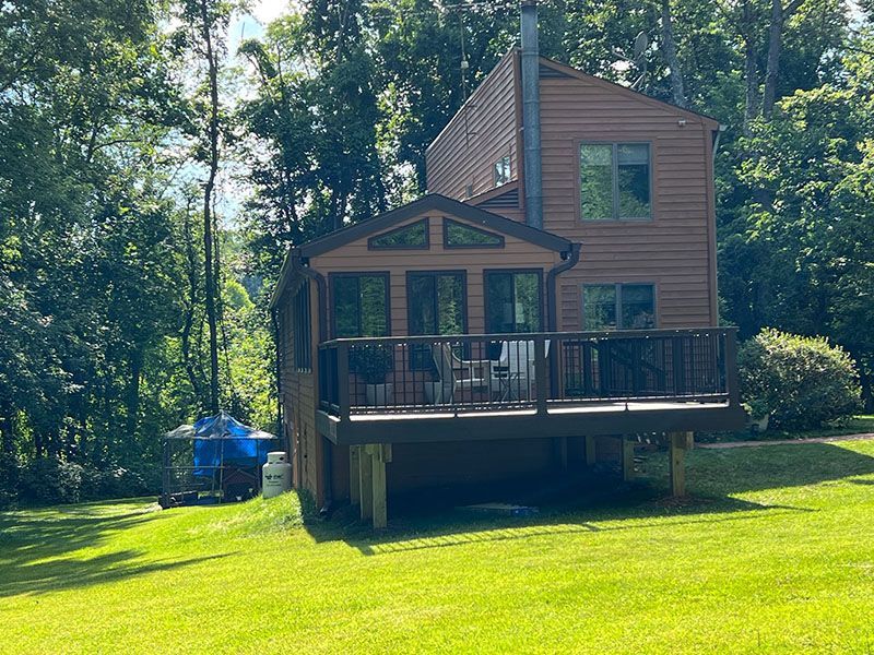 Brown house with a deck, surrounded by trees and a grassy lawn.