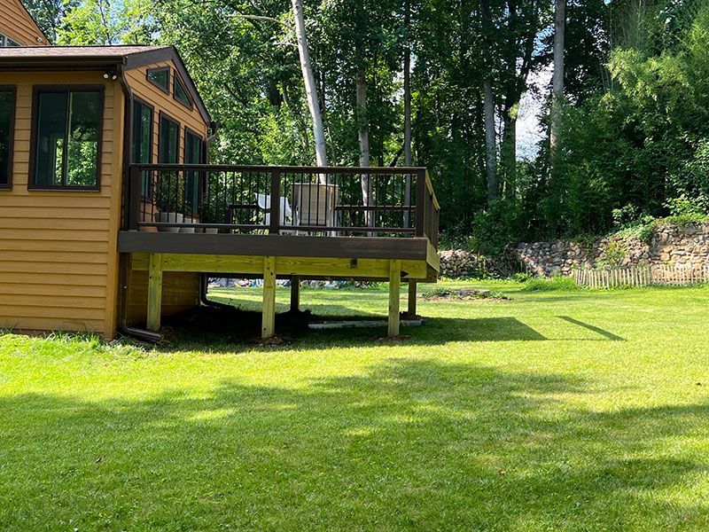 Yellow house with a deck overlooking a green lawn and trees.