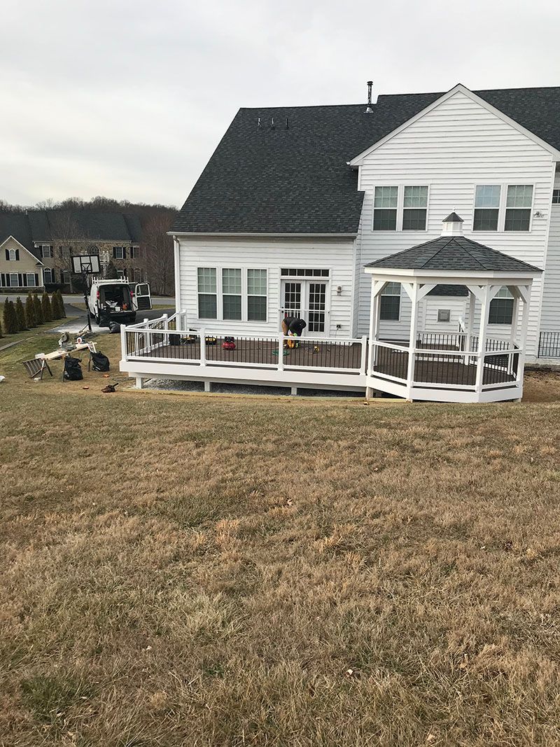 Backyard with white house, deck, gazebo, and brown grass on an overcast day.