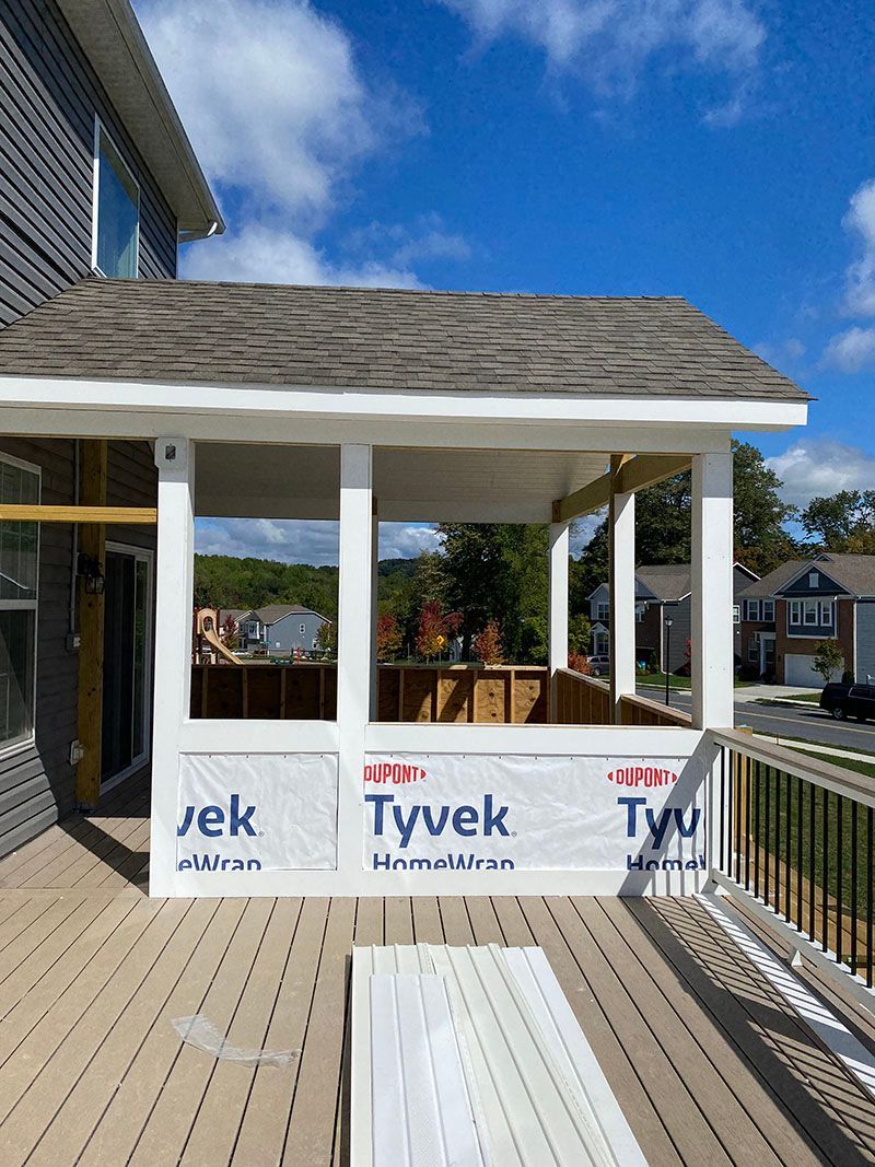 Screened porch under construction on a deck; white trim, Tyvek wrap, grey siding, blue sky.