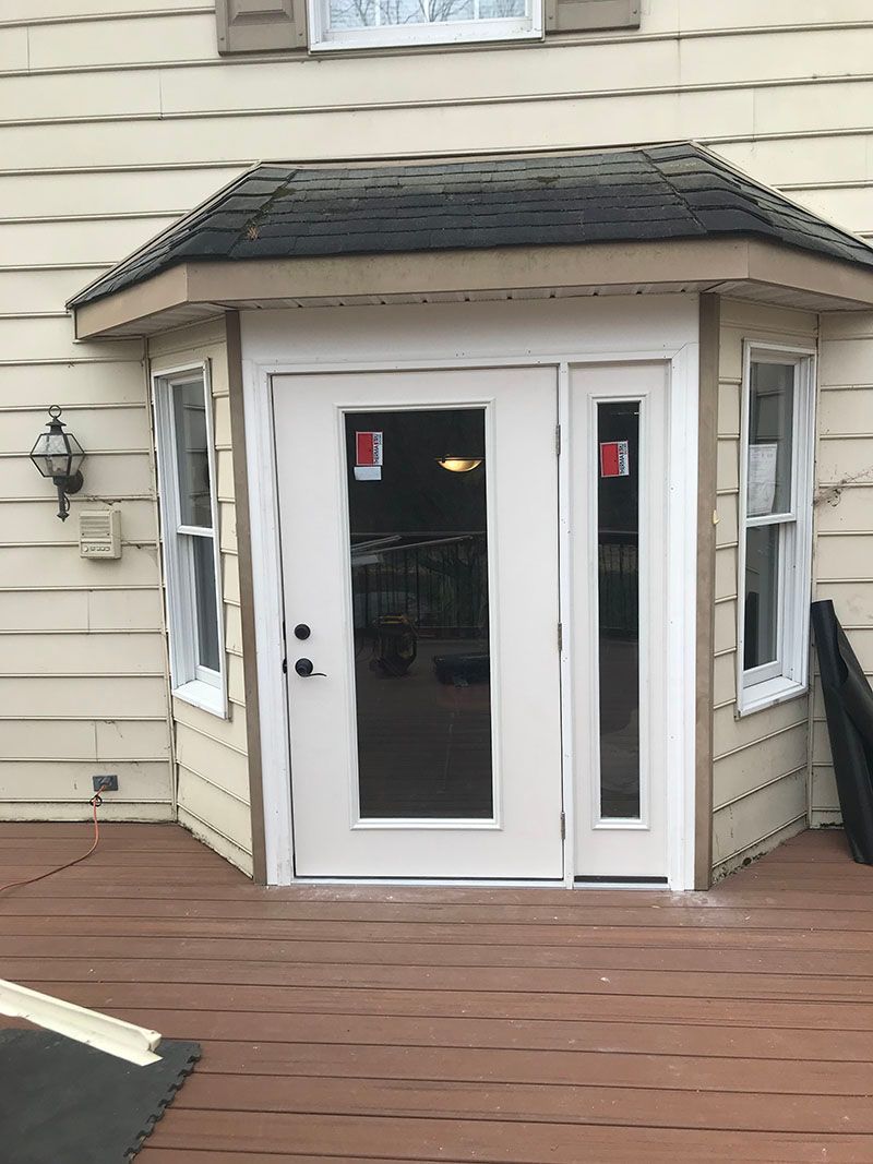 Exterior view of a house with a white door and sidelight on a deck.