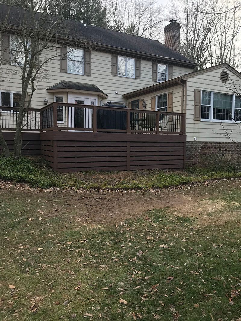 Back view of a two-story house with a wooden deck and brown siding, set in a yard.