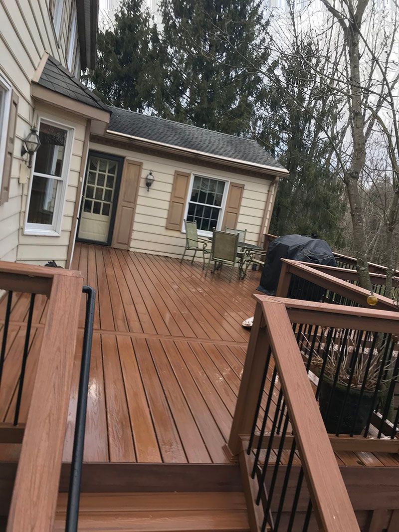 Wooden deck leads to a light-colored shed; trees in the background.