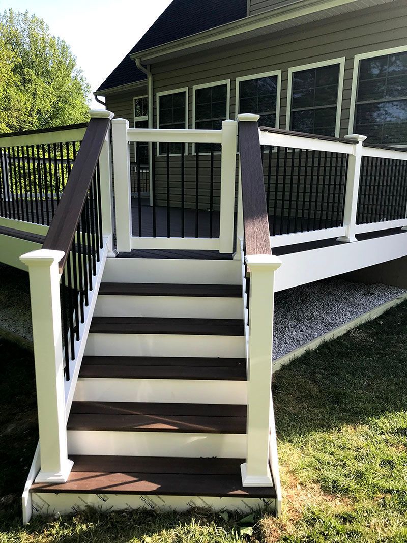 Deck with steps and gate, white and brown composite, black railings, house in background.