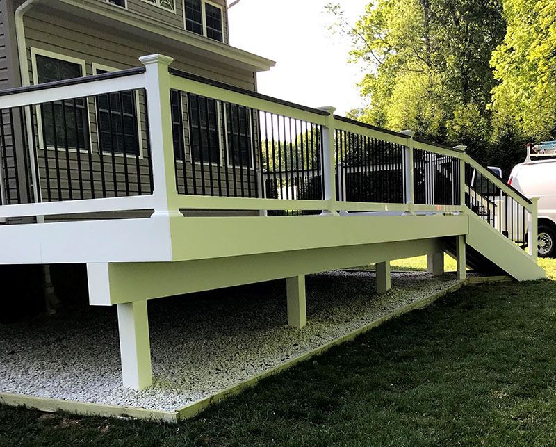 White deck with black railing and stairs next to a house. Gravel bed beneath the deck.