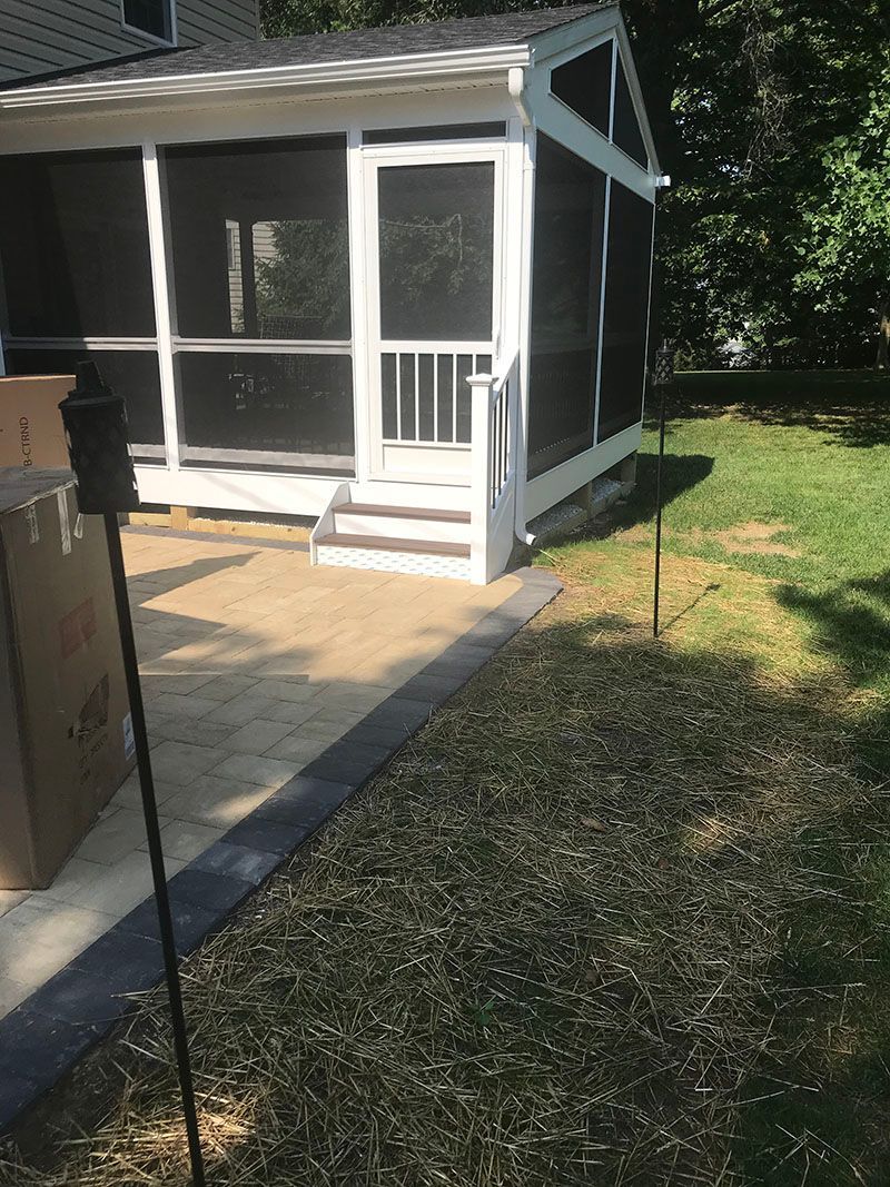 Screened-in porch with white trim, steps, and a concrete patio. Green grass and trees in the background.