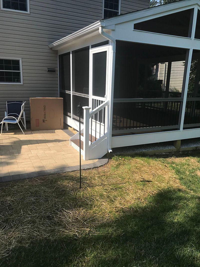 White screened porch and railing next to a house with a grassy yard and concrete patio.