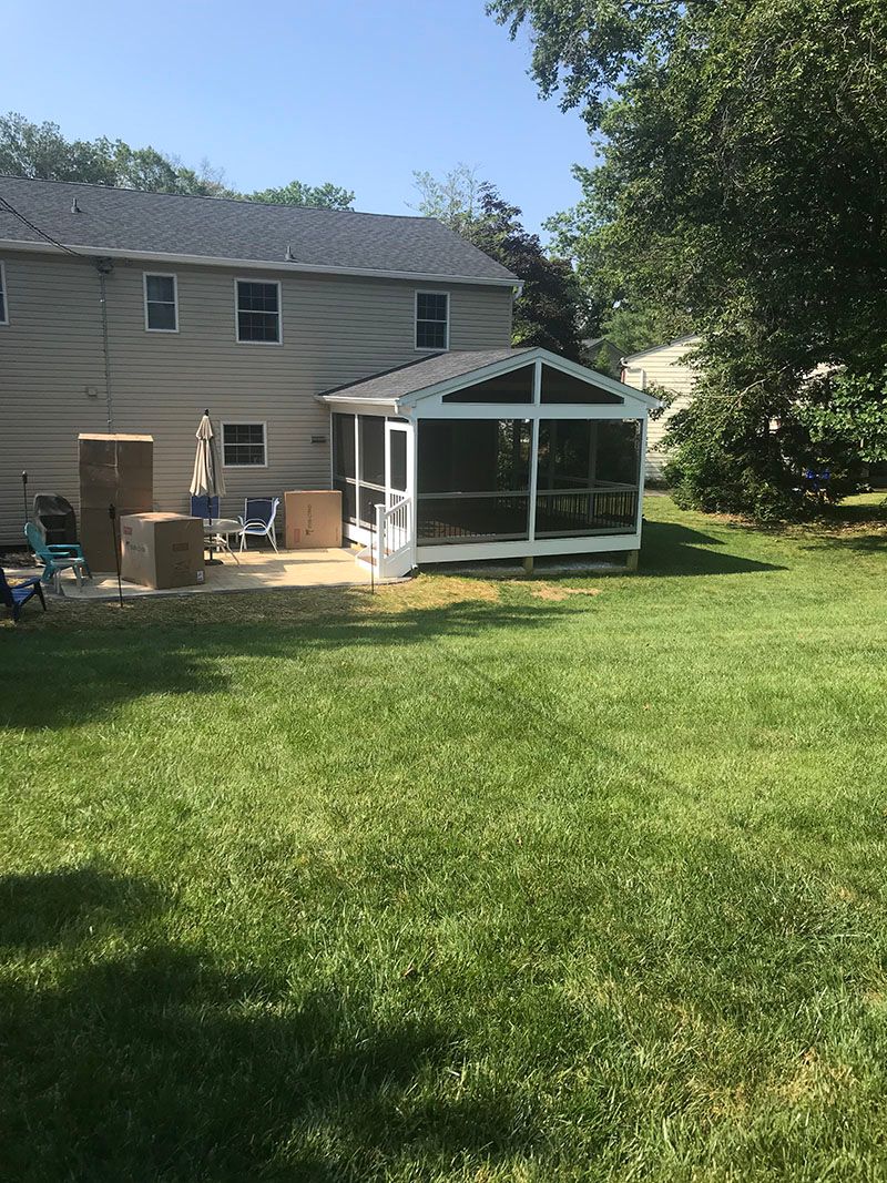 Backyard with a screened-in porch, a house in the background, and patchy grass.