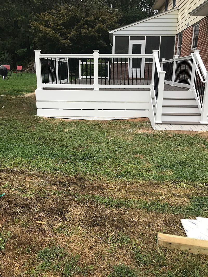 White deck with black railing, steps leading to a house in a grassy yard.