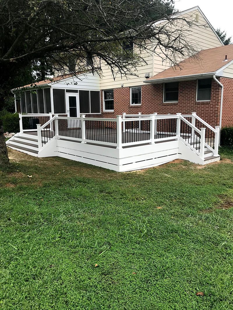 Backyard deck with white trim, black rails, and screened porch attached to a brick house with green grass.