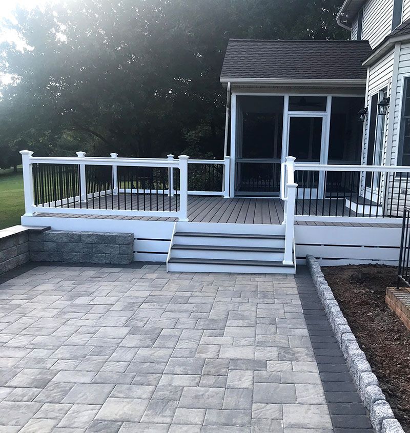 Backyard patio with stone pavers leading to a deck with stairs and a screened porch.