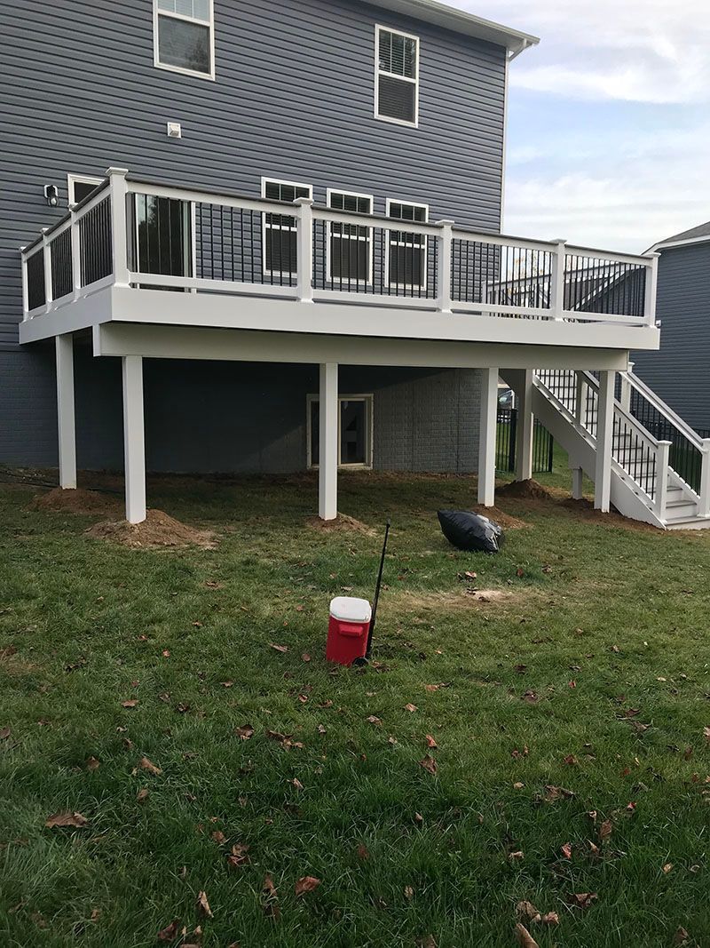 A two-story house with a white deck, overlooking a grassy yard, with a red cooler.