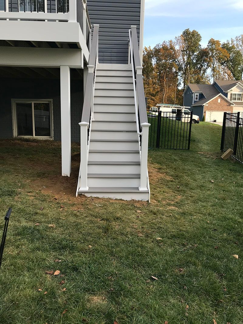 Gray deck stairs leading down to a grassy backyard. White trim, blue siding, and a window are visible.