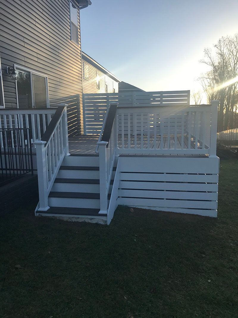 White deck with stairs, railing, and partial wall, attached to a house, on a grassy lawn.