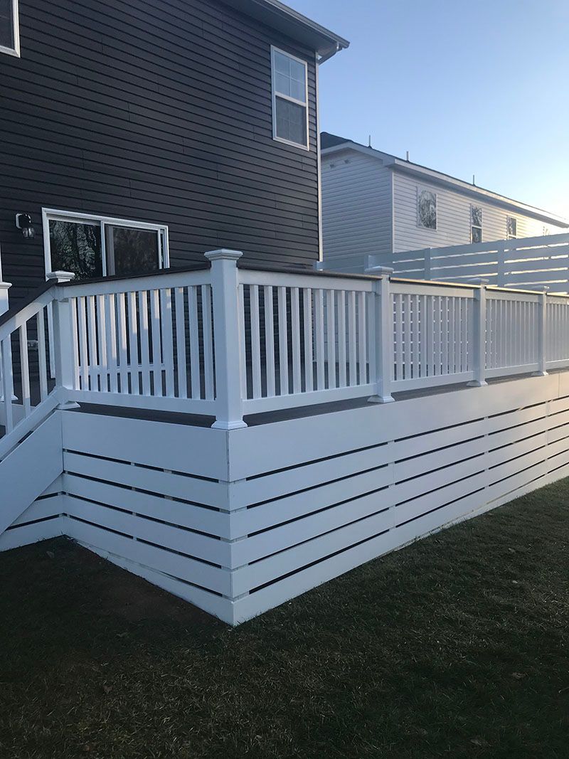 White deck attached to a gray house with matching railings. Bright, sunny day.