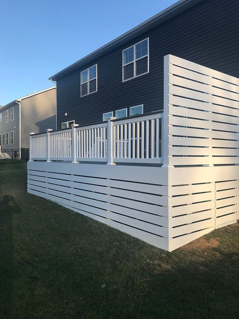 White deck with horizontal slat privacy fence attached to a dark blue house on a grassy lawn.