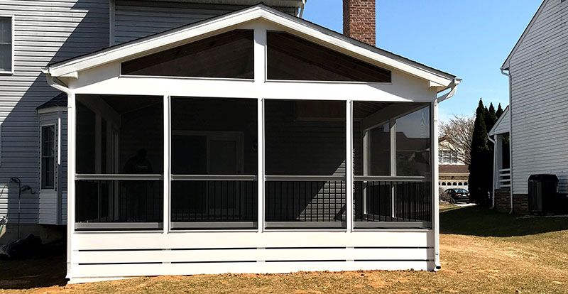 Screened-in porch attached to a house, with white frame and black railing, in a grassy backyard.