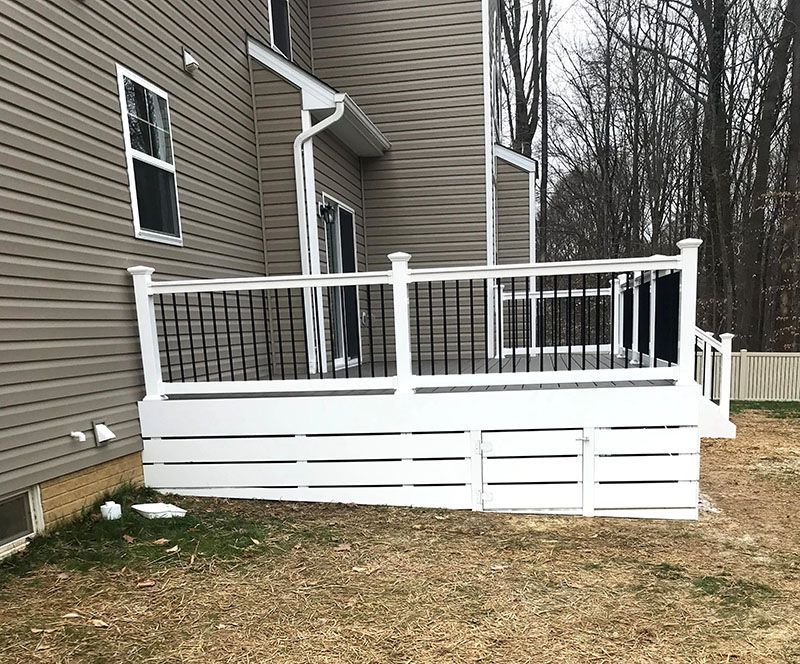 White deck with black railings attached to a house with tan siding; wooden backyard.