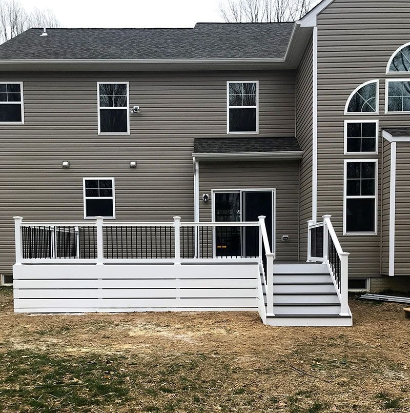 A two-story house with a new white deck and stairs. Gray siding, dark windows. Bare yard.