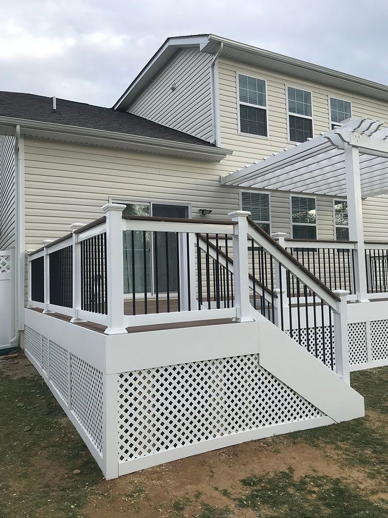 A two-story house with a white deck and latticework, black railings, and a pergola.