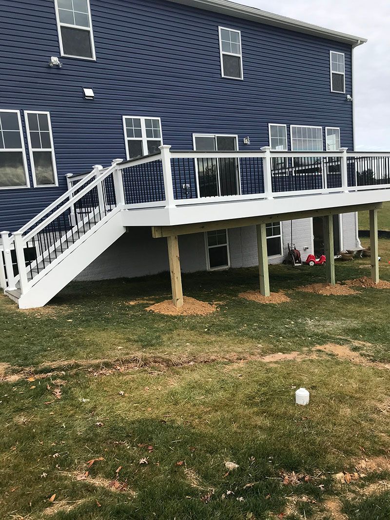 Two-story house with blue siding and a white deck. A set of stairs leads down to the lawn.
