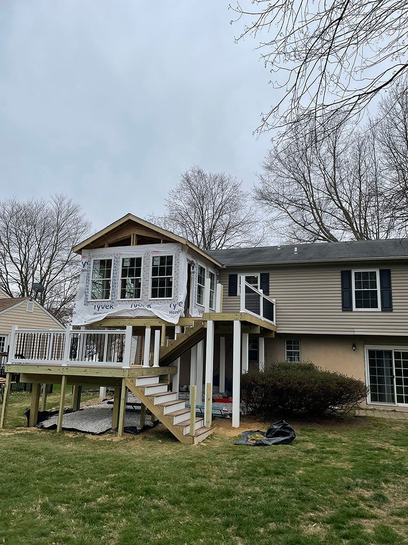 Backyard with a partially built deck and sunroom addition to a tan house on a cloudy day.