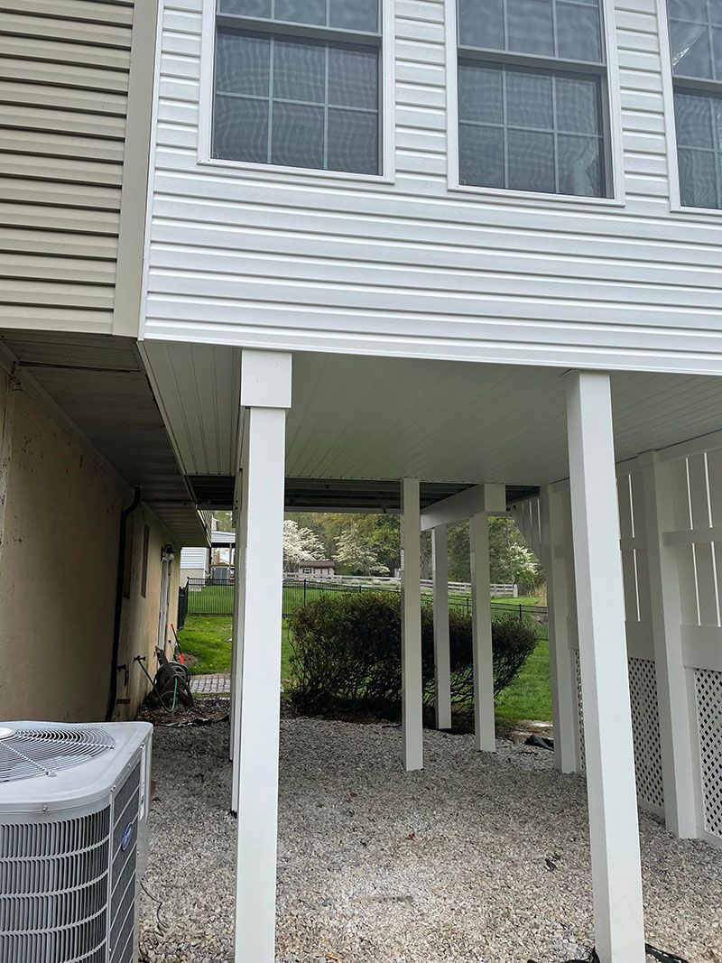 White deck supported by posts; an air conditioner sits below.