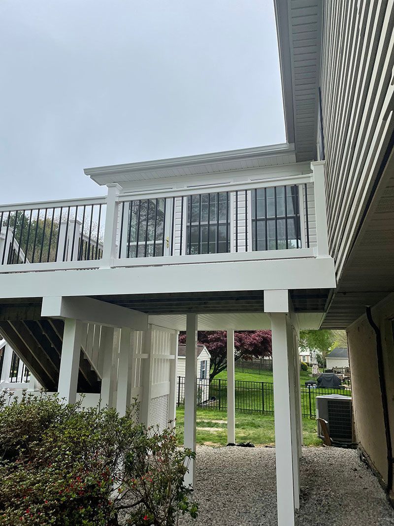 White painted deck with railings and posts, overlooking a yard with green grass and trees.