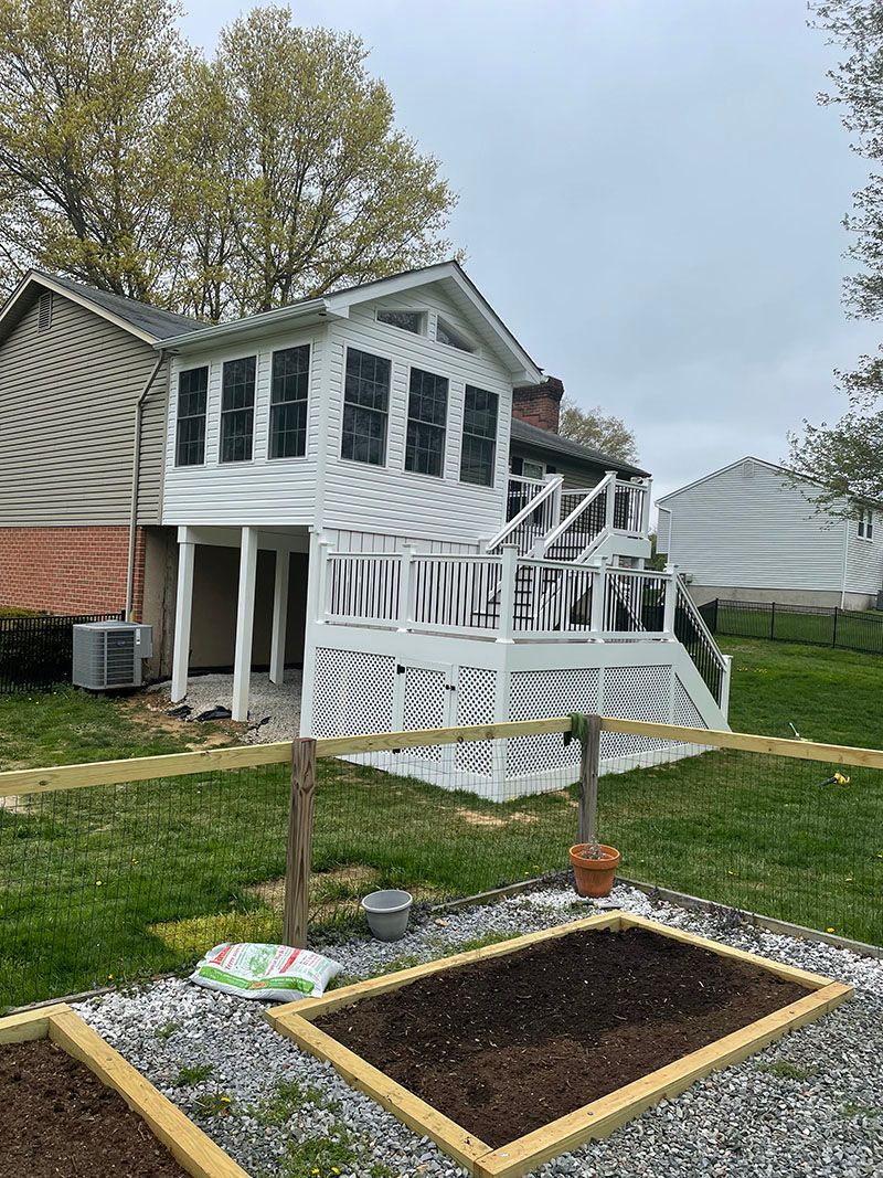 A white deck and sunroom attached to a house, with a small garden in the foreground.
