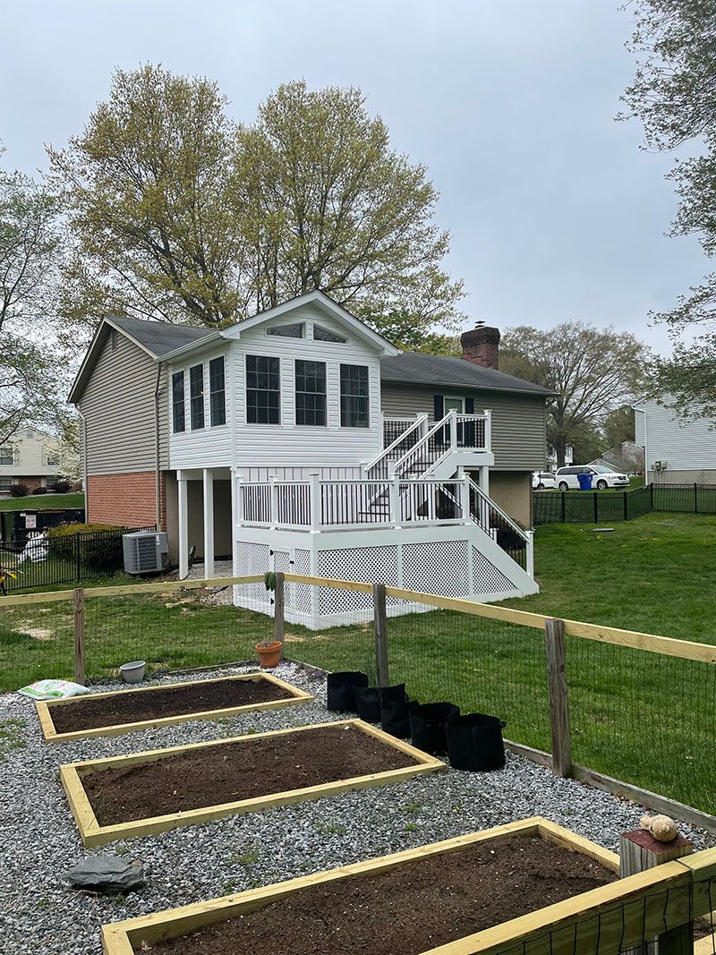 Backyard with a white deck attached to a house, a raised garden bed, and a wooden fence.
