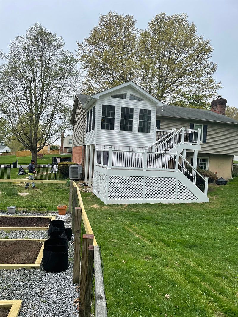 White and tan house with a deck, next to a garden. Overcast sky.